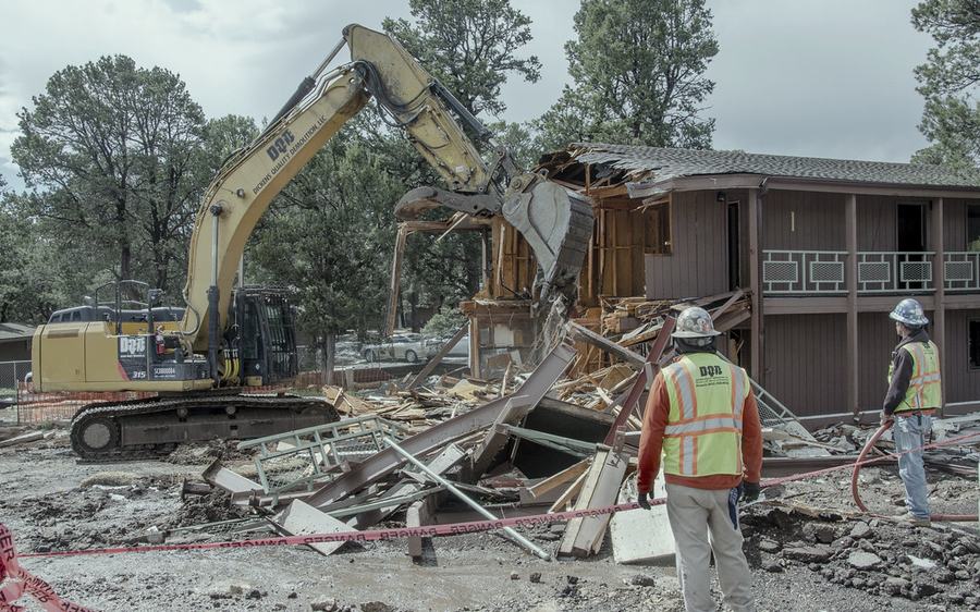 An excavator at work while a spotter in a high-visibility vest watches