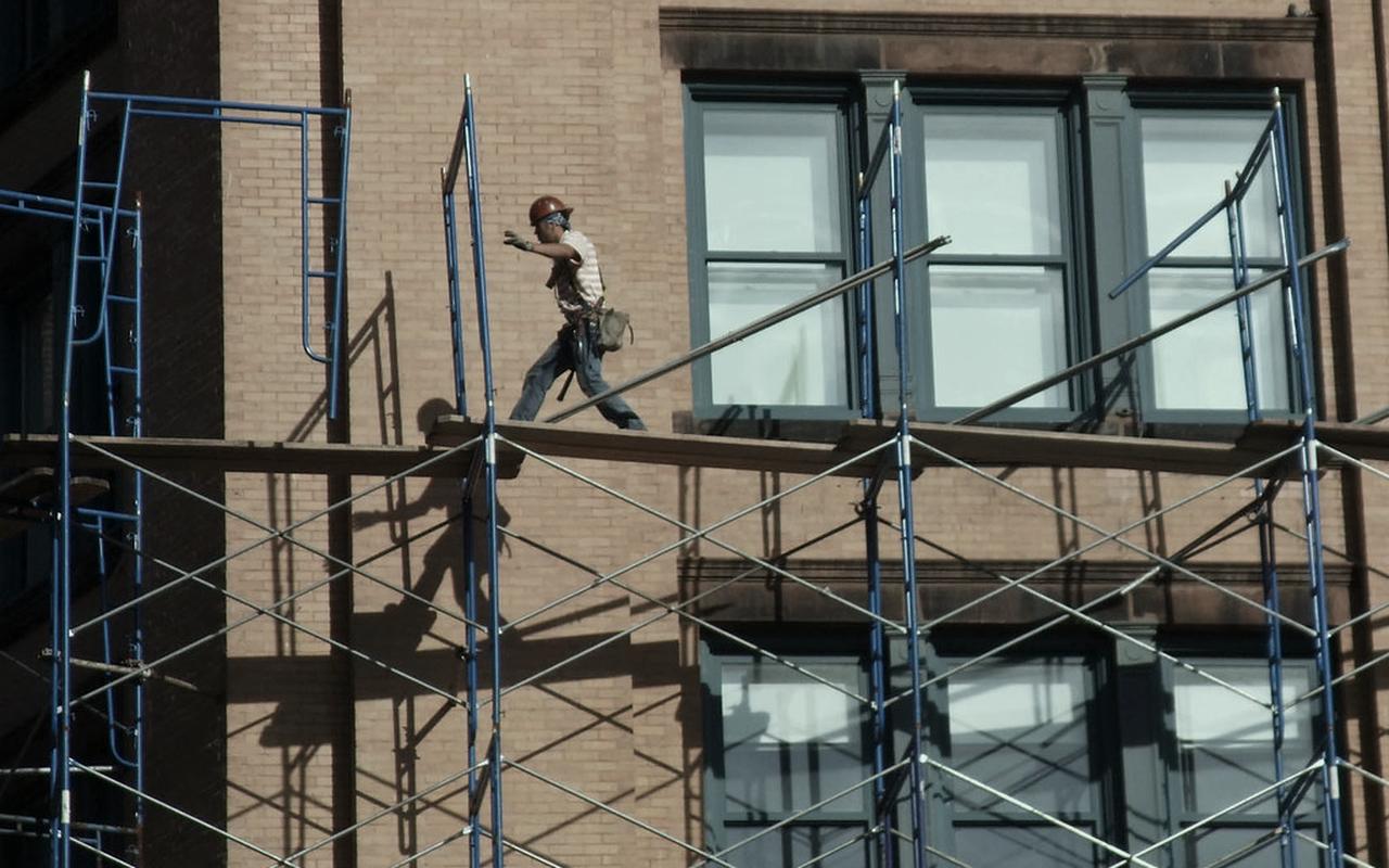 Workers moving along scaffolding against a brick facade