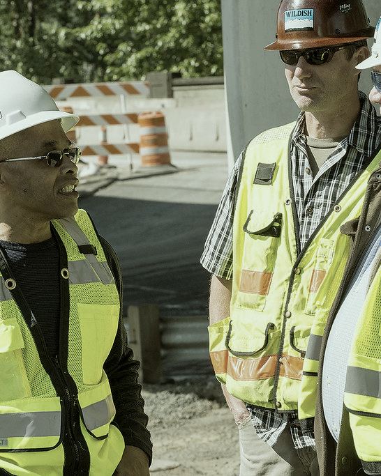 Two construction workers in hard hats and high-visibility vests talking on site